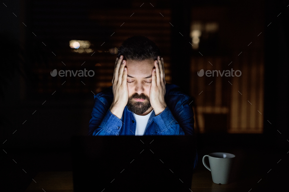A tired man with laptop at home at night. Stock Photo by halfpoint