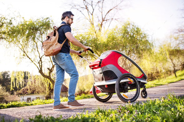 A father with jogging stroller on a walk outside in spring nature.