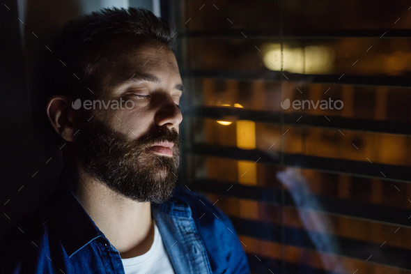 A man slepping by the window at home at night. Stock Photo by halfpoint