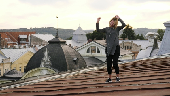 Woman Feeling Happy while Listening to Music on Headphones Dancing on Rooftop alt