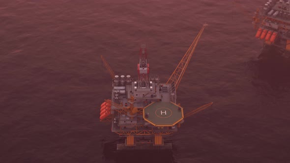 Two offshore platforms in the open sea with a pink evening sky and setting sun. alt