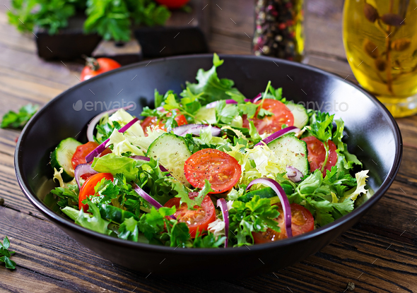 Salad from tomatoes, cucumber, red onions and lettuce leaves. - Stock Photo - Images