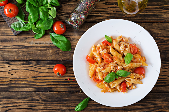 Penne pasta in tomato sauce with chicken, tomatoes, decorated with basil on a wooden table - Stock Photo - Images