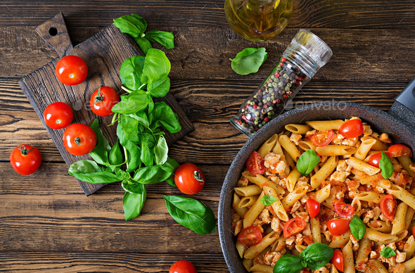Penne pasta in tomato sauce with chicken, tomatoes, decorated with basil on a wooden table. - Stock Photo - Images