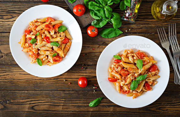 Penne pasta in tomato sauce with chicken, tomatoes, decorated with basil on a wooden table. - Stock Photo - Images