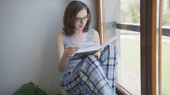 Young Woman Sitting in Window at Home and Reading alt