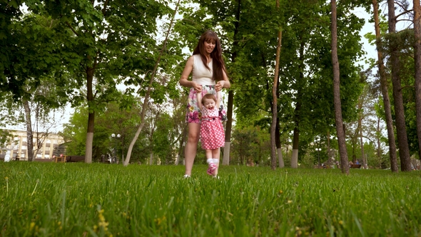Mom Is Shaking Hands in Air with a Happy Laughing Daughter. Parent Plays with Baby on Green Grass in alt