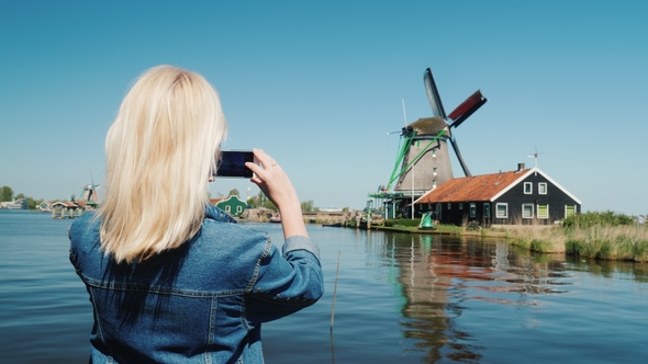 A Woman Tourist Takes Pictures of Old Windmills in Holland. Travel and Tourism in Europe alt