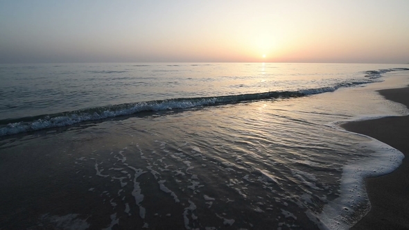 Calm Waves of the Sea on the Sandy Beach at Sunset. Sun Reflection in Sea Water. Nature Background
