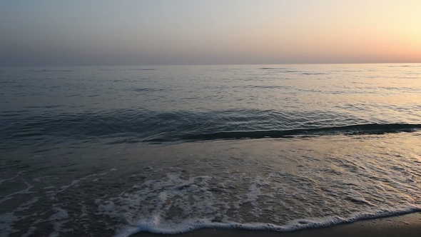 Calm Waves of the Sea on the Sandy Beach at Sunset. Sun Reflection in Sea Water