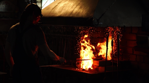 Blacksmith Fanning the Flames of the Furnace Using the Tools Prevents Embers alt