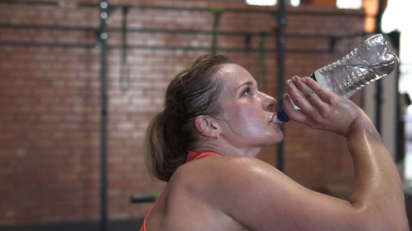 Tired Sweaty Fitness Woman Drinks Water From a Bottle During Workout in Gym