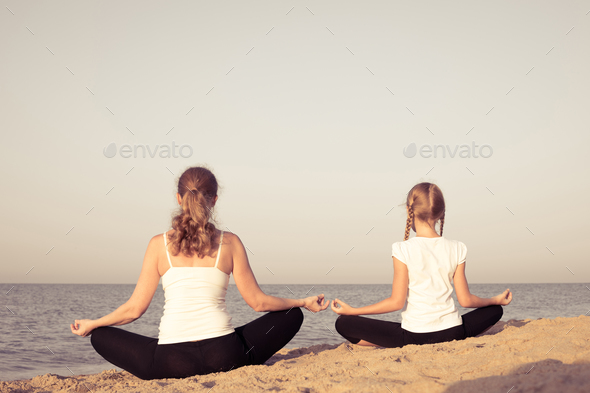 Mother with daughter doing a yoga exercise on the beach stock photo