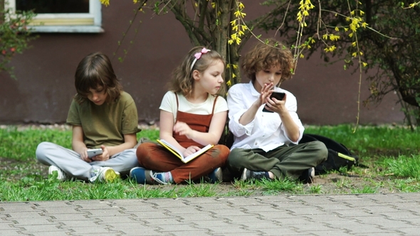 The Girl Is Reading a Book, the Boys Are Playing Games in Smartphones. The Schoolgirl Is Upset alt