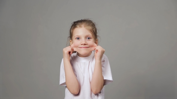 Cute Young Girl Playing the Ape. Funny Girl Showing Grimaces Over Grey Background