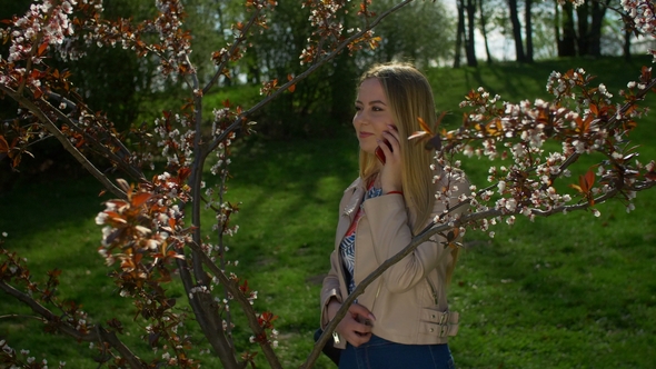 Happy Young Woman Chatting on Smart Phone in Park alt