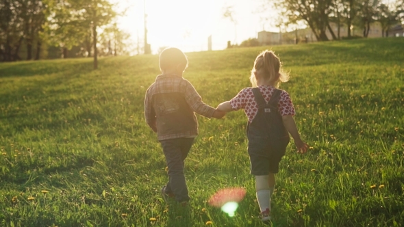 Little Boy and Girl Walking Together Along Summer Field at Sunset