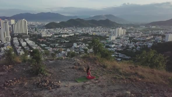 Woman Does Yoga in Lotus Pose Against City Near Mountains