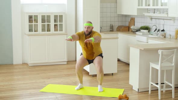 Bearded Fat Sweaty Man in Yellow Wet Sportswear Doing Squats Exercise at Home