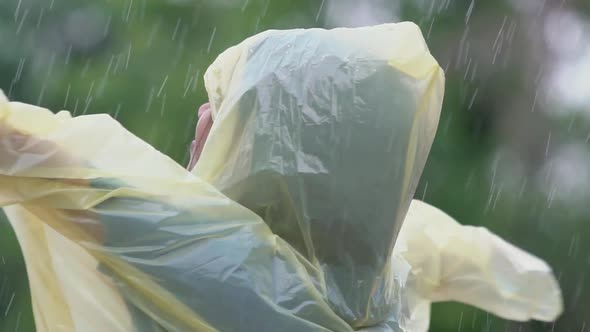 Asian girl wearing yellow raincoat enjoying rainfall. Kid playing splashing on outdoors, Slow motion