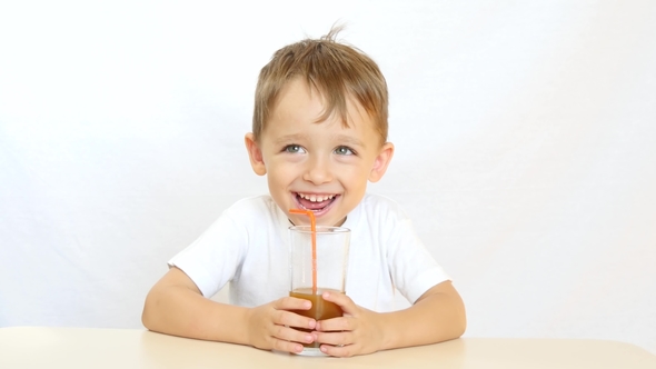 A Happy Child Is Drinking Juice Through a Straw, Sitting at a Table and ...