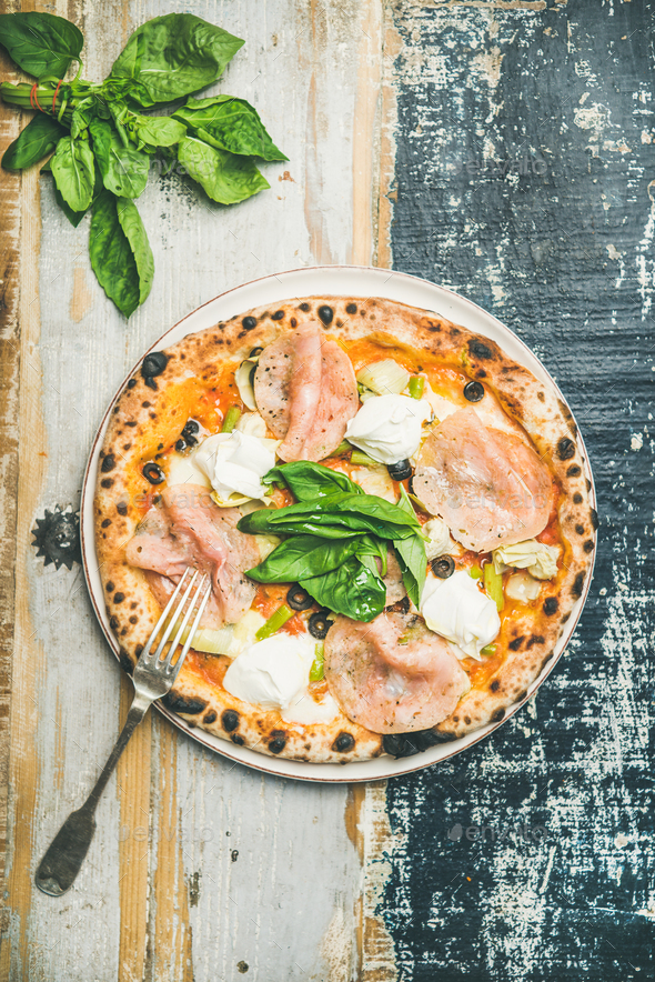 Freshly baked pizza with ham, artichokes, cheese, basil on plate - Stock Photo - Images