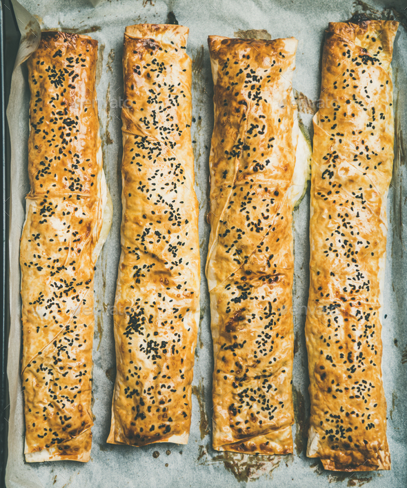 Flat-lay of freshly baked Turkish borek pastry rolls with spinach - Stock Photo - Images