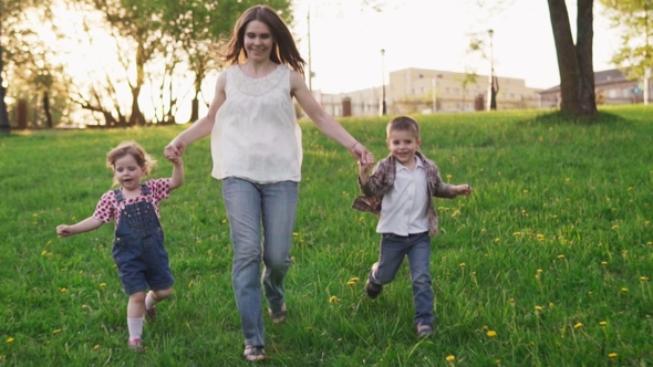 Happy Mother and Children Holding Hands Running Together and Smiling in Park