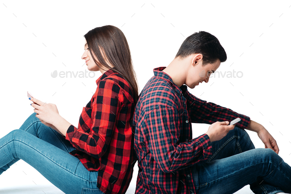 Couple sitting back to back and using phones - Stock Photo - Images