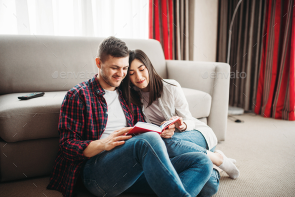 Couple sitting on floor and looks at book together - Stock Photo - Images