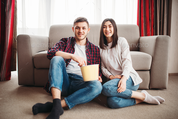Couple sitting on floor and watch tv with popcorn - Stock Photo - Images