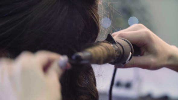 Hands of Stylist Curling Hair with Curling Tongs