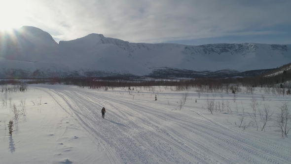 Man Is Hiking in Mountains in Sunny Winter Day and Using Hiking Poles. Aerial View alt