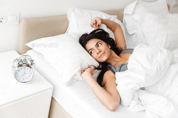 Portrait of pleased relaxed woman stretching in bed at bedroom w - Stock Photo - Images