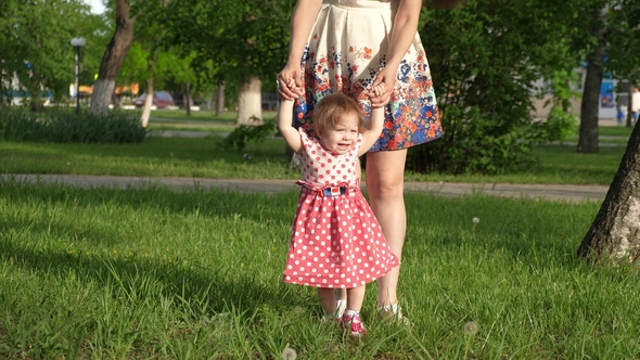 Mum Walks in Park on Lawn with Small Child, Mom Teaches To Walk Little Daughter alt