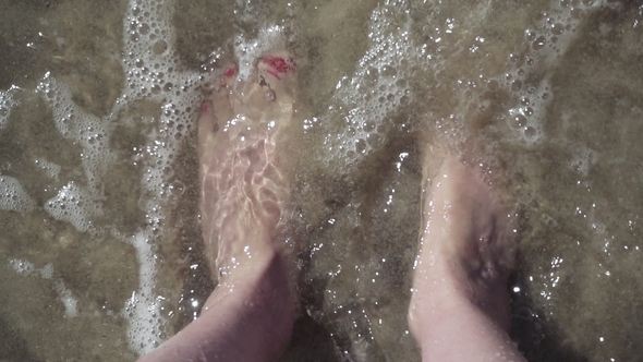 Female Feet in Clear Sea Water on Beach. Toes with Beautiful Red Pedicure