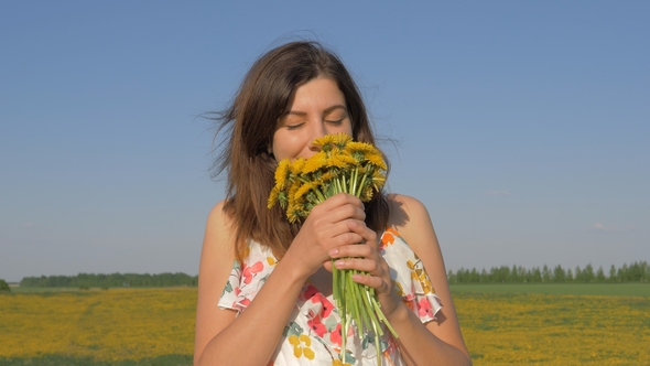 Portrait of Woman In Field With Bouquet of Yellow Dandelion Flowers Sniffing Him alt