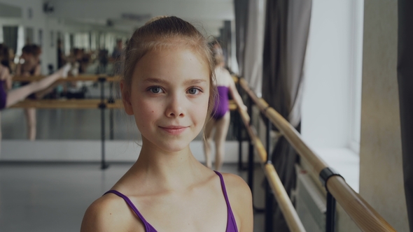 Portrait of Beautiful Little Girl in Bodysuit Standing in Ballet Class, Smiling and Looking alt