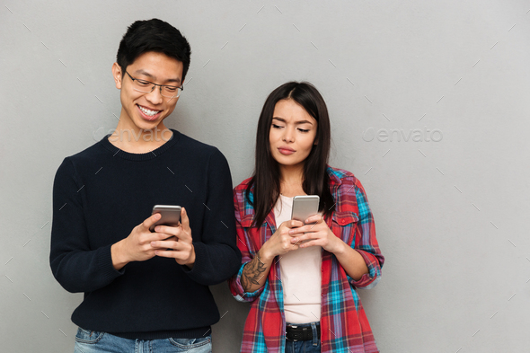 Young asian loving couple using mobile phones. Stock Photo by vadymvdrobot
