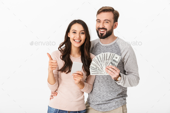 Happy young loving couple holding money showing thumbs up using mobile phone. - Stock Photo - Images