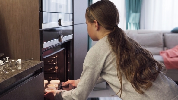 Girl Puts Cupcakes in Oven for Baking in Kitchen at Home alt