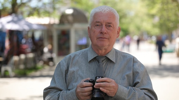 Auld Man Stands, Raises His Camera and Takes Photos in an Airy Street