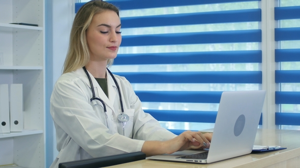 Smiling Nurse Typing On Laptop And Making Notes At Reception Desk By Play Preview