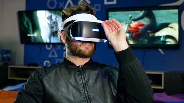 Young Man Views an Object in Virtual Reality Through Special Glasses. The Bearded Man Picks Up the