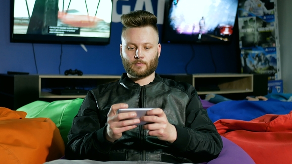 Bearded Guy Who Plays on a Smartphone Is Offered To Take a Joystick and He Takes It and the Phone