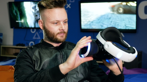 Young Man Looks at Virtual Reality Glasses Holding Them in His Hands