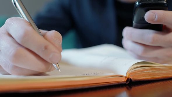 of Male Hands Holding Telephone and Taking Notes in Notebook alt