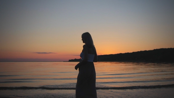 Beautiful Silhouette Pregnant Girl at Sunset Goes on Beach