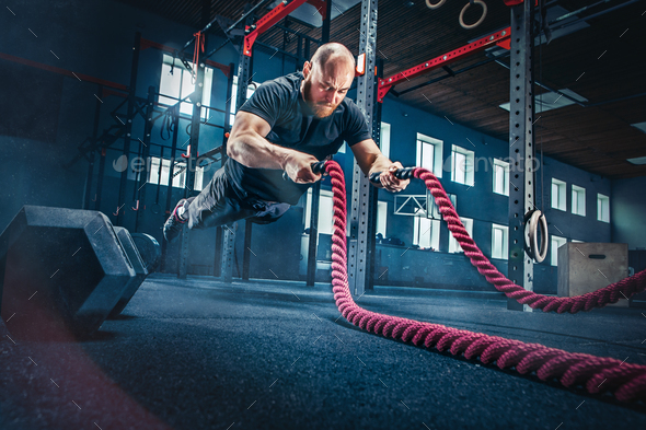 Men with battle rope battle ropes exercise in the fitness gym. Stock Photo by master1305