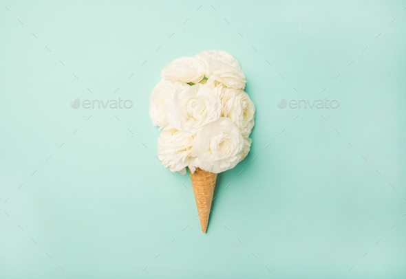 Waffle cone with white buttercup flowers over blue pastel background - Stock Photo - Images